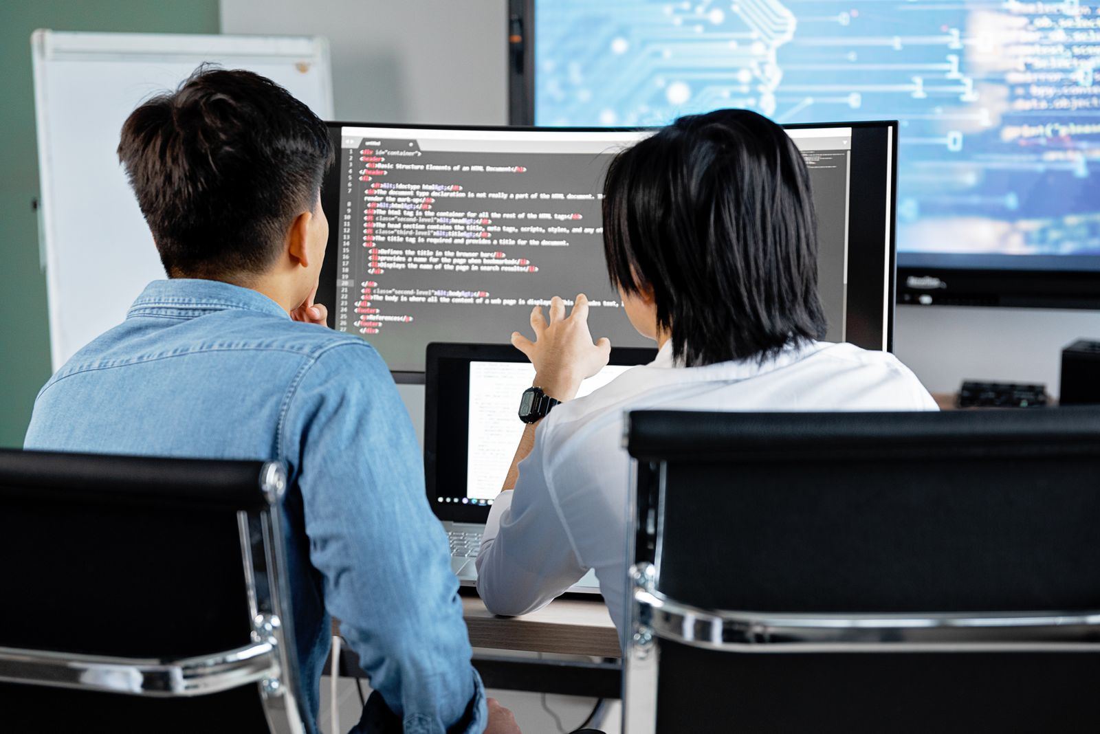 Two developers examining code together on a large monitor.