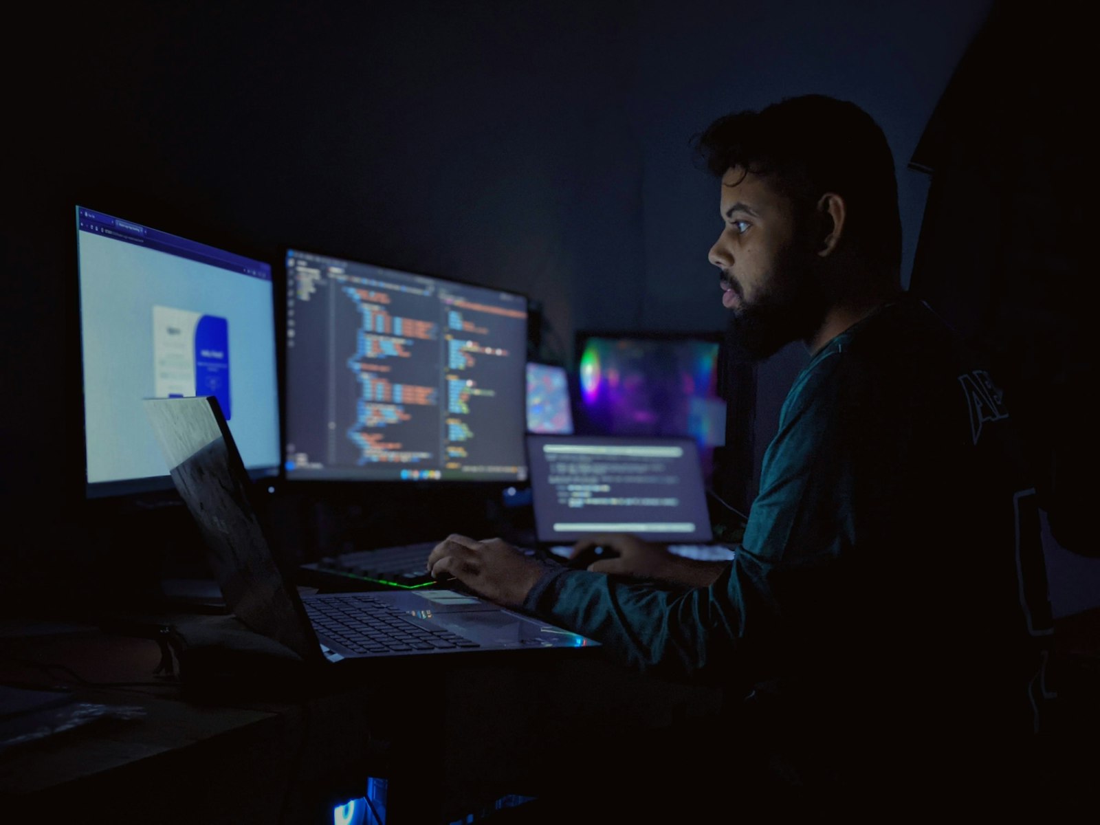 A developer working at several code-filled screens in a softly lit workspace.