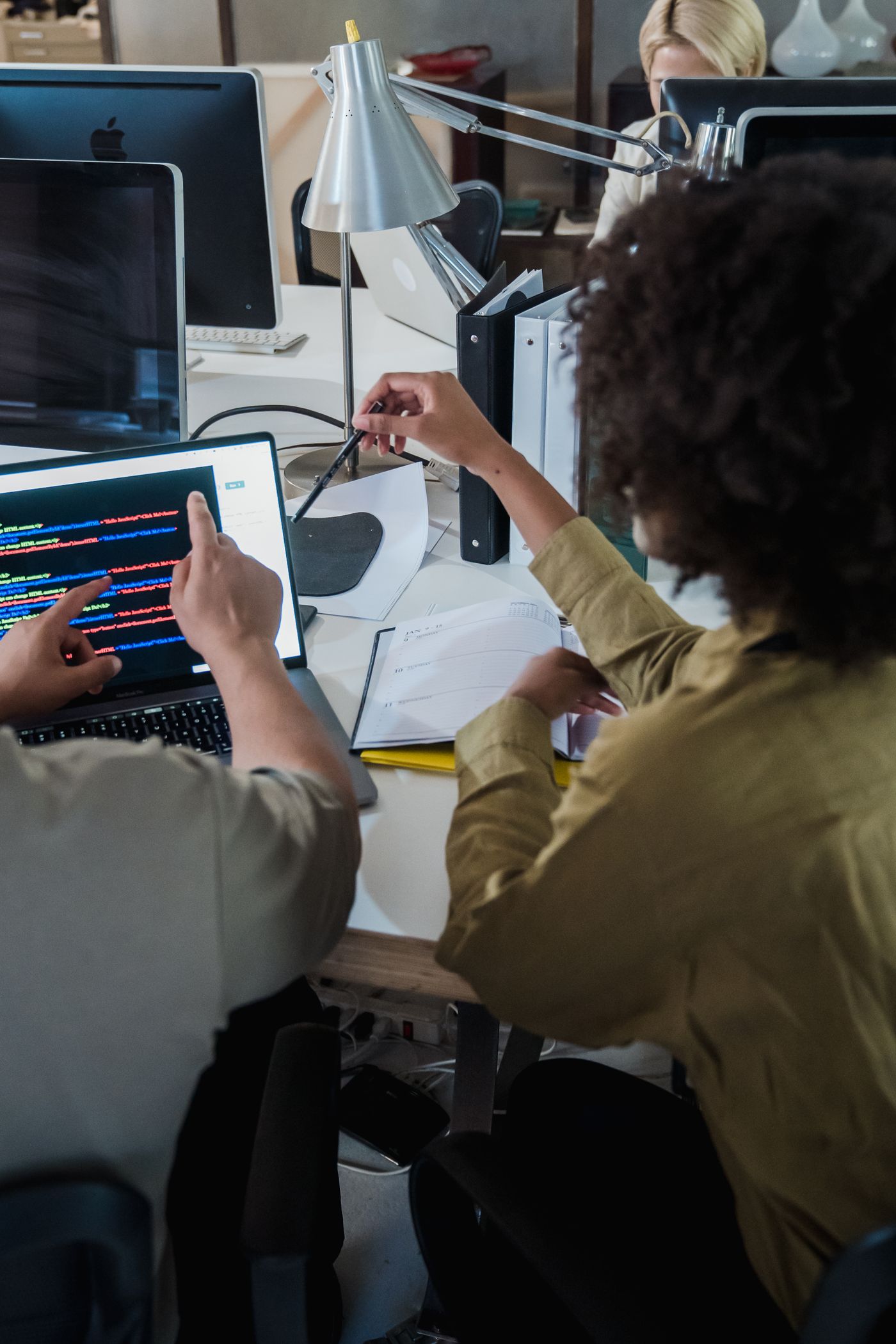 Colleagues pointing out details in code during a laptop review.